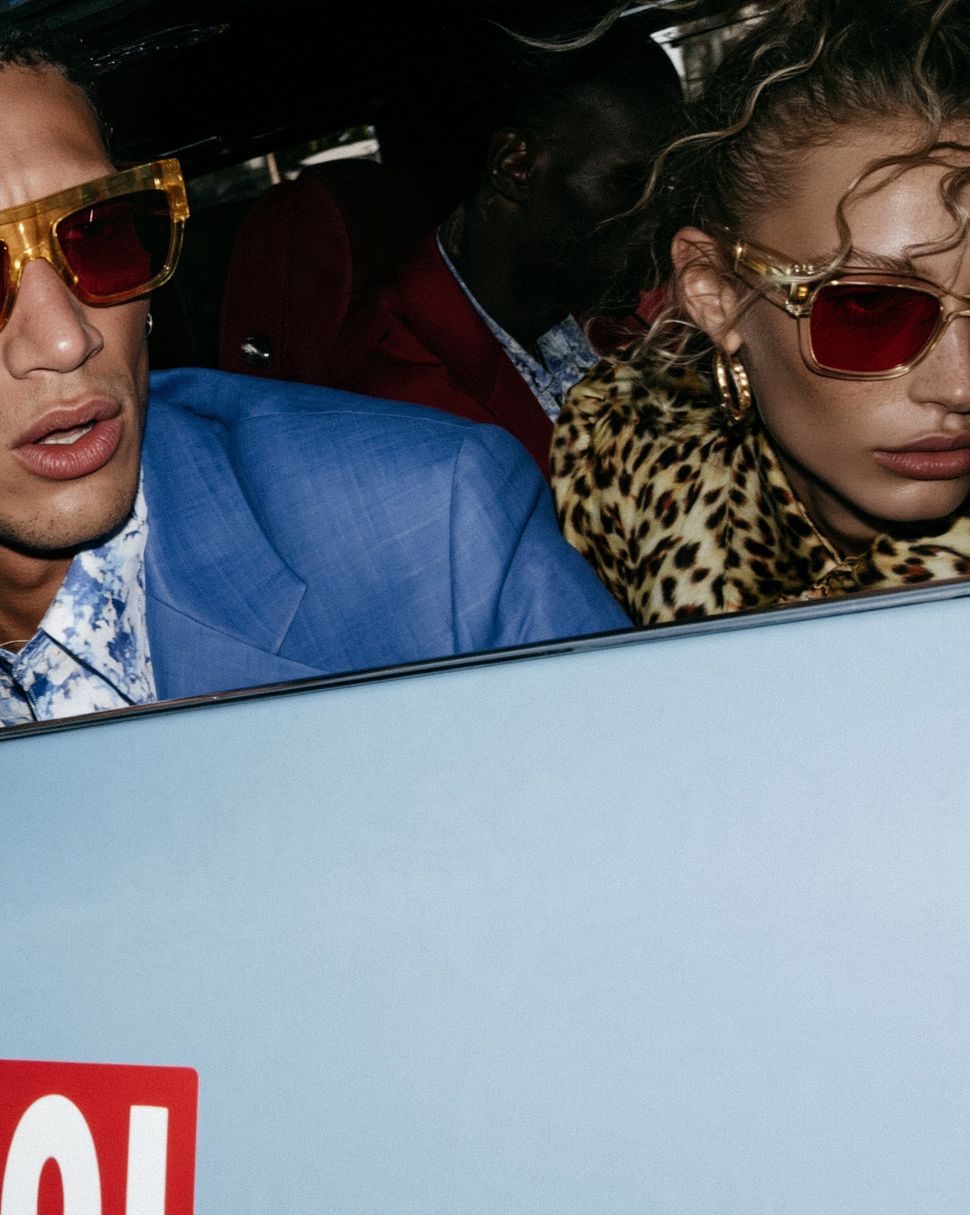 In Transit — Models wearing red-tinted sunglasses, a blue blazer, and leopard print looking out a light blue car window