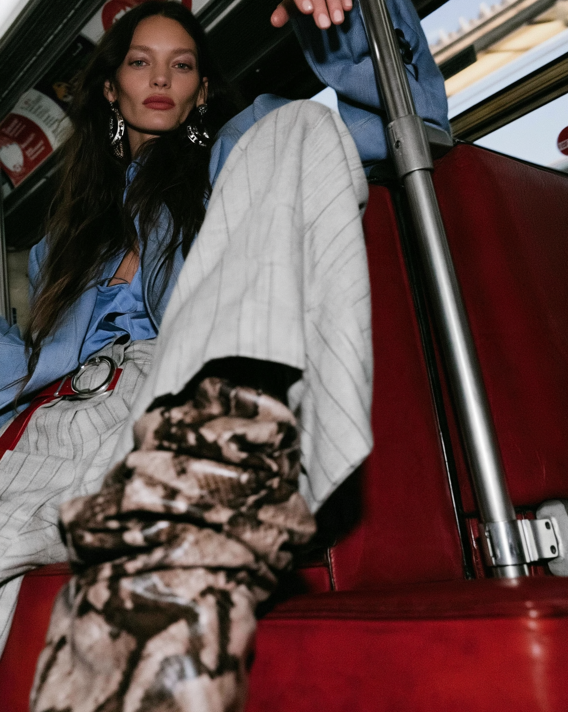 In Transit — Low-angle shot of a woman in a blue shirt, pinstripe trousers, and snakeskin boots on red transit seats